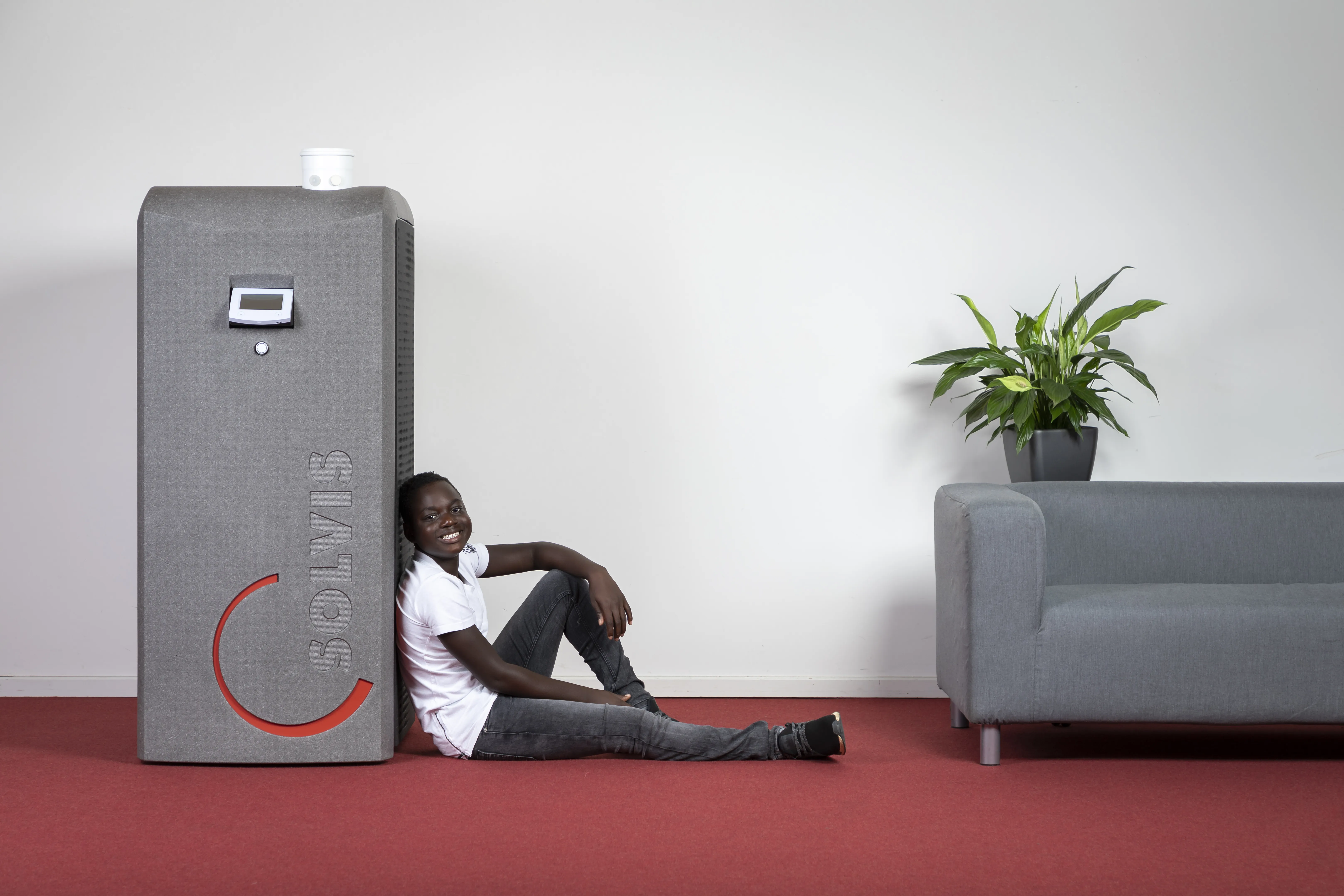 Junge sitzt angelehnt an einem Kompakt-Heizkessel SolvisBen. 