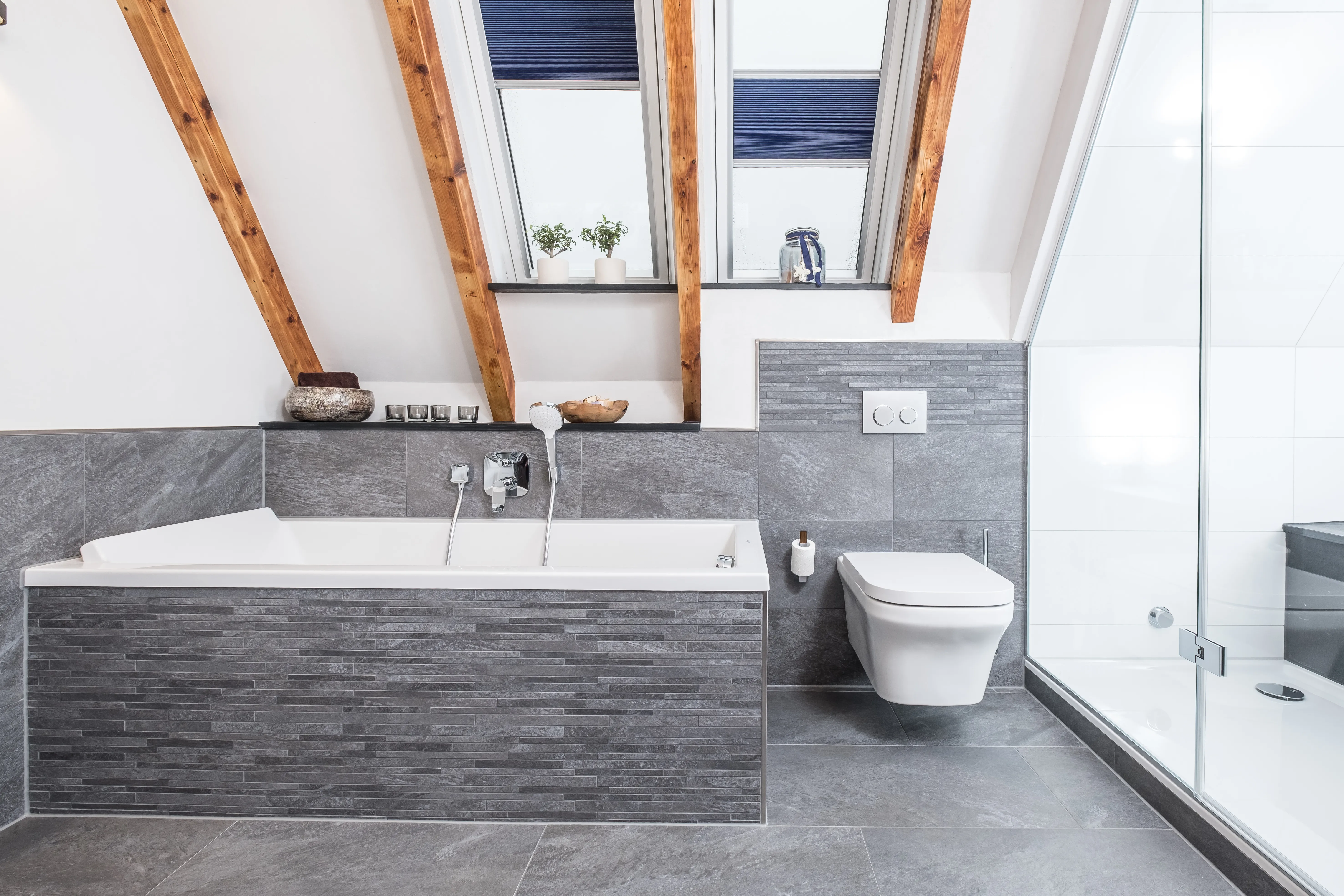 Moderne Badewanne mit grauer Natursteinverkleidung unter Dachschräge und Dachfenstern.