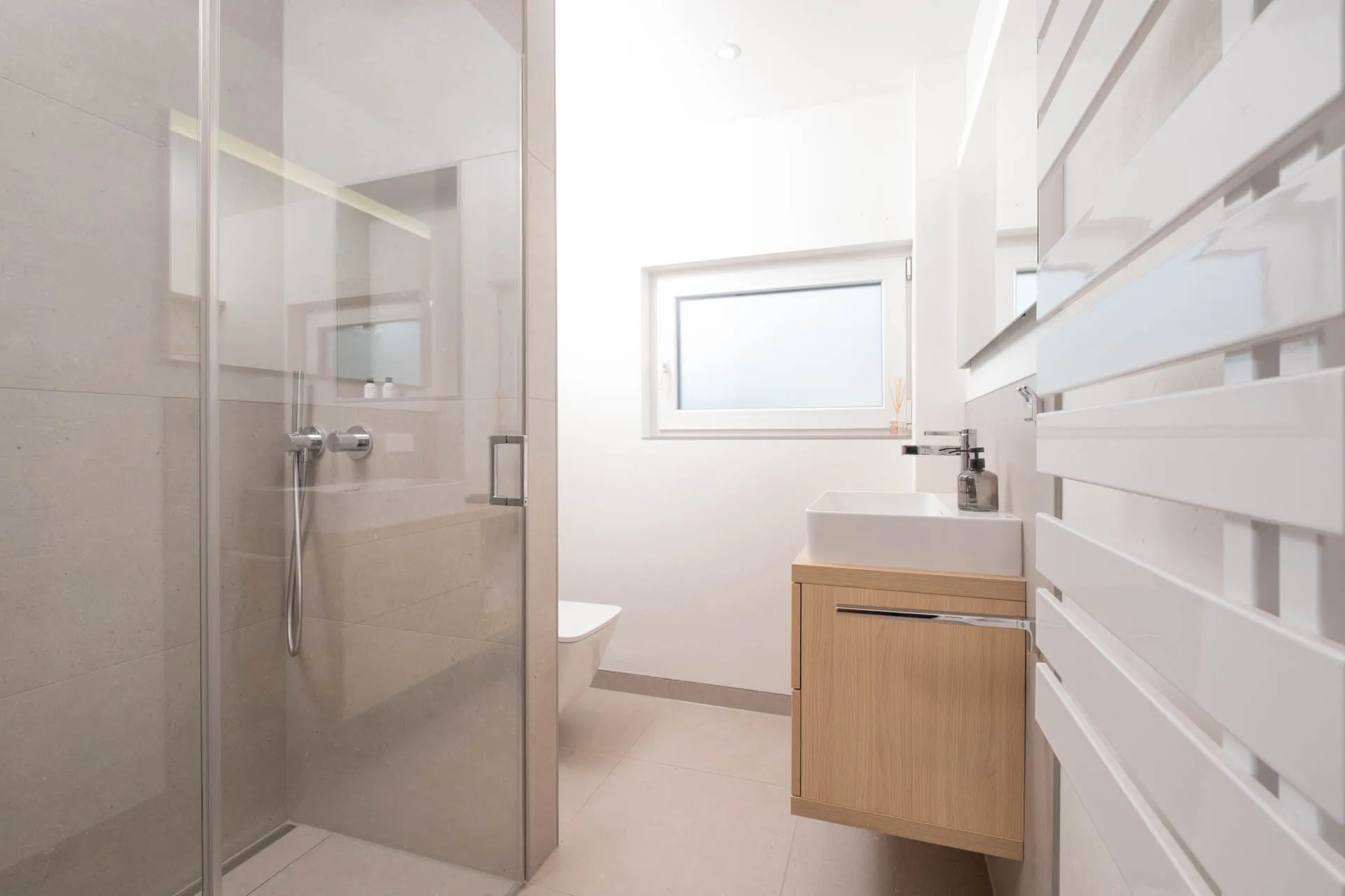 Kleines modernes Badezimmer mit bodengleicher Dusche, Glasabtrennung und hellem Holzwaschtisch.