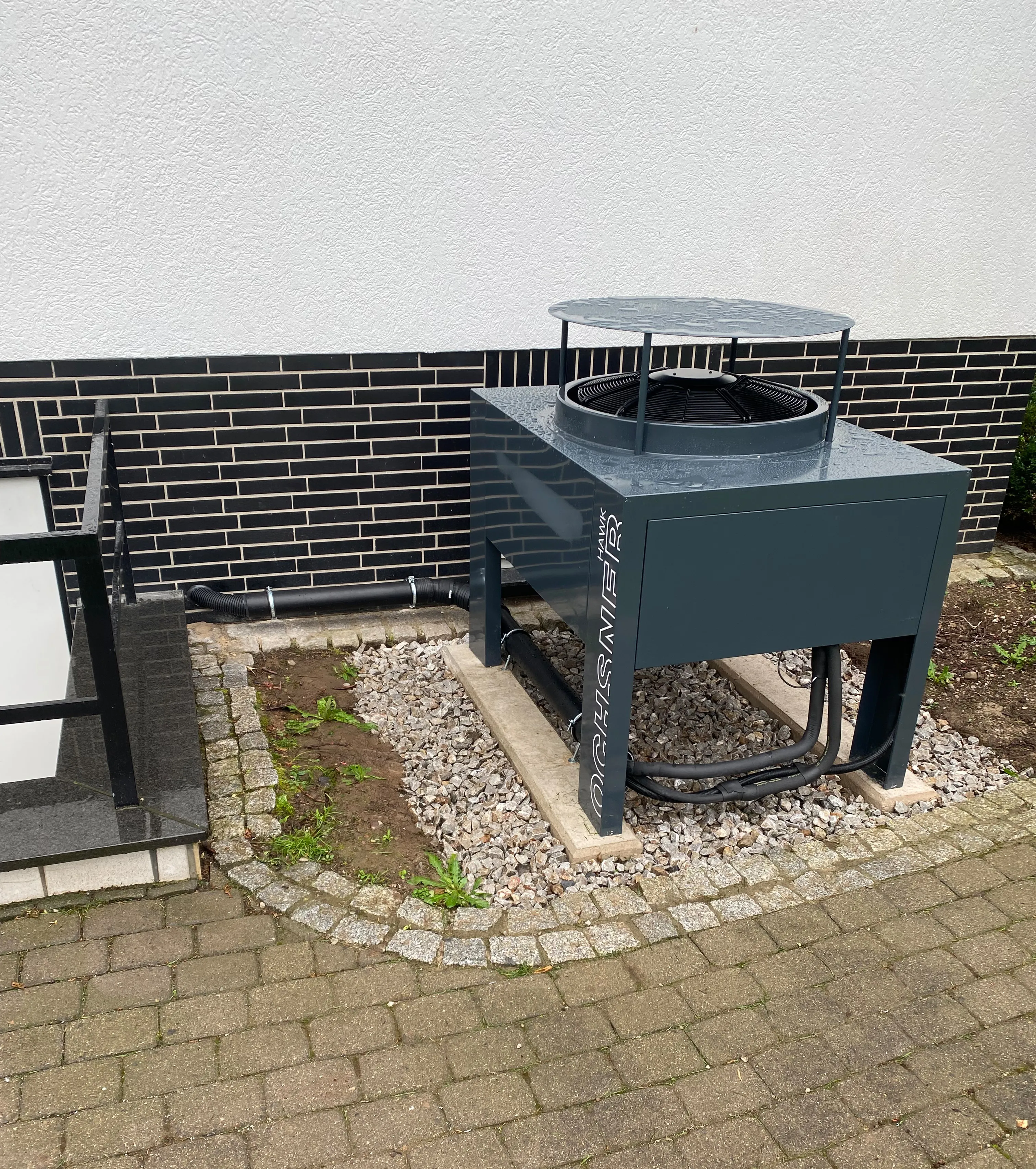 Außengerät einer Wärmepumpe im Garten neben Hauswand installiert.
