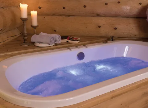 Whirlpool im Kerzenlicht in einem Badezimmer mit Holzverkleidung und blauem Farblicht im Wasser.. 