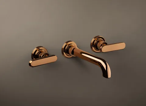 Eine Wandarmatur der Serie Frattini Parklane in glänzendem Roségold ist auf einer matten Wand montiert.