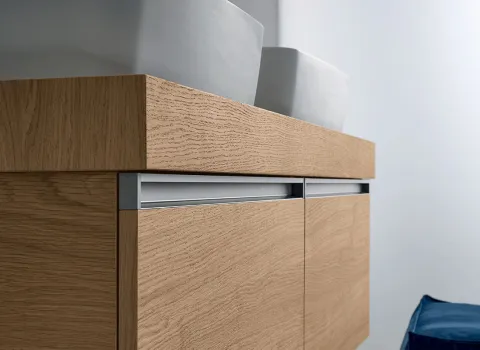 Detailansicht eines Stocco Badmöbels mit heller Holzfront, integrierter Griffleiste und aufgesetztem Waschbecken.