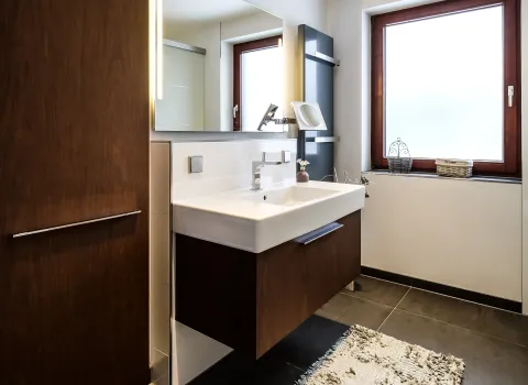 Badezimmer mit Waschtisch, Fenster und dunklen Bodenfliesen.