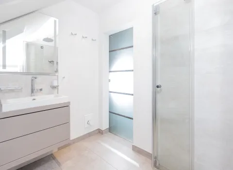 Helles Dachbad mit schwebendem Waschtischunterschrank, Spiegel und moderner Glasdusche.