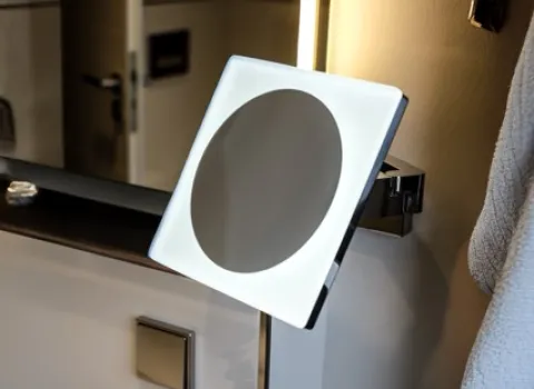 Beleuchteter Kosmetikspiegel mit LED-Rahmen auf Glasablage im modernen Badezimmer.