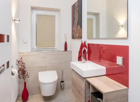 Modernes Badezimmer mit roter Glasrückwand, Waschtisch mit Holzunterschrank und wandhängendem WC.