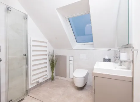 Modernes Badezimmer mit Dachschräge, bodengleicher Glasdusche, wandhängendem WC und hellem Waschtisch mit großem Spiegel.