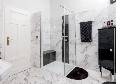 Moderne Glasdusche in Marmorbad mit schwarzem Badschrank.