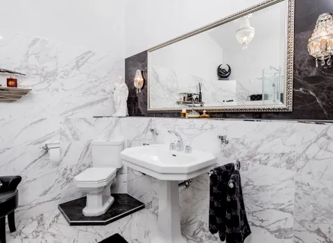 Klassisches Badezimmer mit Marmorfliessen, Waschtisch und großem Wandspiegel.