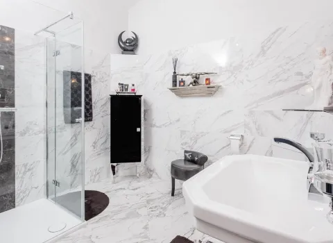 Luxuriöses Badezimmer mit Marmorfliessen, Glasdusche und schwarzem Badschrank.