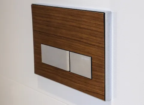 Detailaufnahme einer Spülkastenbetätigung in Holzoptik mit Chromtasten.