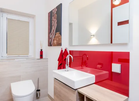 Waschtisch mit Aufsatzbecken, großem Spiegel und roter Glasrückwand in modernem Bad.