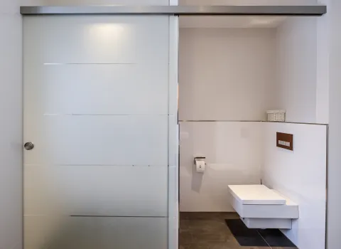 WC-Nische mit wandhängendem WC und Spülkastenbetätigung in Holzoptik.