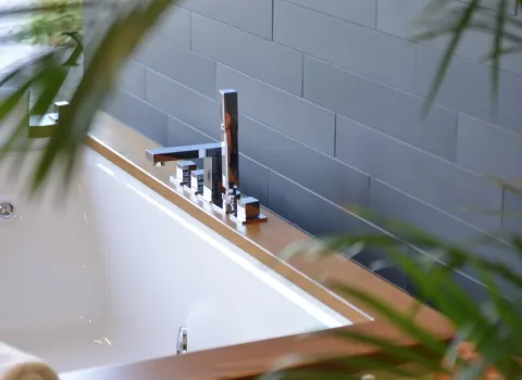 Detailaufnahme einer Badewanne mit moderner Armatur, Kerzen und Pflanze im Hintergrund.