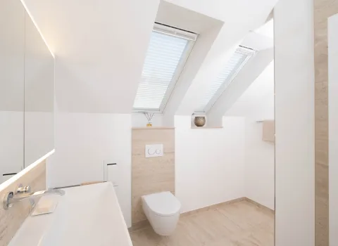 Helles Badezimmer mit Dachschräge, Waschtisch und beleuchtetem Spiegelschrank mit LED.