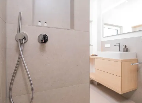 Blick von der Dusche auf modernen Holzwaschtisch mit Aufsatzbecken und Spiegel.