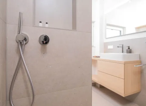 Blick von der Dusche auf modernen Holzwaschtisch mit Aufsatzbecken und Spiegel.