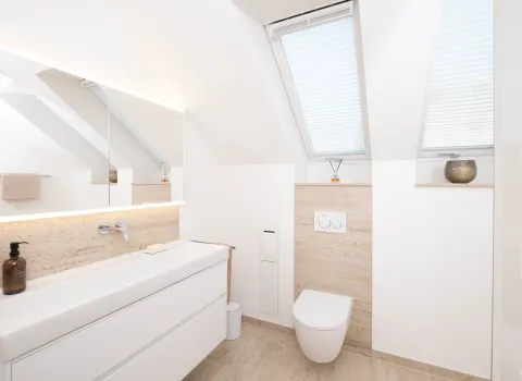 Dachbad mit schwebendem Waschtisch, LED-Spiegelbeleuchtung und Travertin-Wandverkleidung.