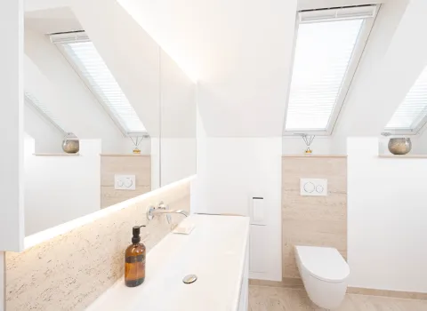 Modernes Dachgeschoss-Badezimmer mit Waschtisch, Wand-WC und Travertin-Naturstein unter Dachschräge.