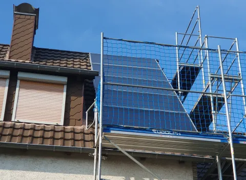 Dachsanierung an Einfamilienhaus mit Baugerüst und neuem Dachaufbau unter blauem Himmel.
