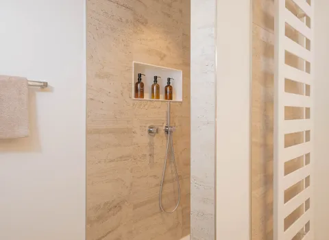 Walk-In-Dusche mit Regendusche und großformatigen Travertin-Wandfliesen.