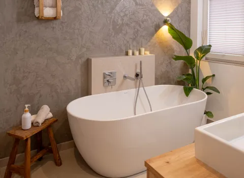 Freistehende Badewanne mit dekorativer Pflanze und strukturierter Wand im Badezimmer.