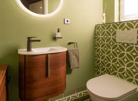 Modernes Gäste-WC mit grünen Wänden, gemusterten Fliesen und Holzwaschtisch.