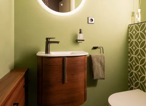 Waschbecken im Gäste-WC mit rundem LED-Spiegel und grüner Wandgestaltung.