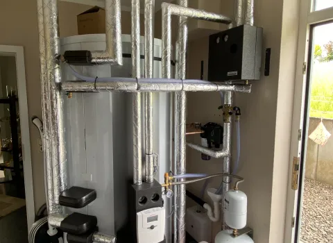 Heizungsanlage mit Pufferspeicher und umfangreichen isolierten Rohrleitungen im Technikraum.