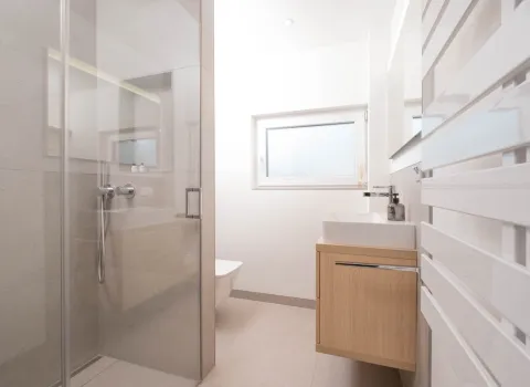 Kleines modernes Badezimmer mit bodengleicher Dusche, Glasabtrennung und hellem Holzwaschtisch.