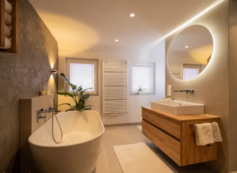 Modernes Badezimmer mit freistehender Badewanne, Holzwaschtisch und rundem LED-Spiegel.