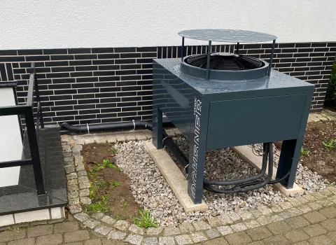 Außengerät einer Wärmepumpe im Garten neben Hauswand installiert.