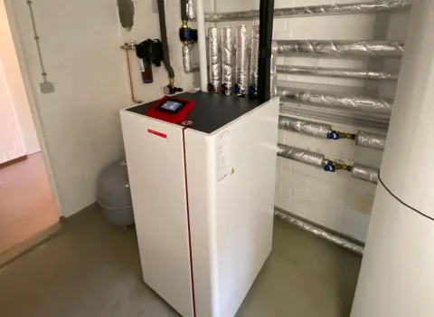 Innenmodul einer Wärmepumpe mit angeschlossenen Leitungen im Technikraum.