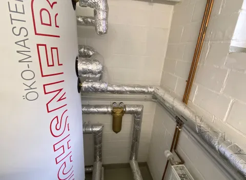 Warmwasserspeicher mit isolierten Rohrleitungen im Heizungsraum.