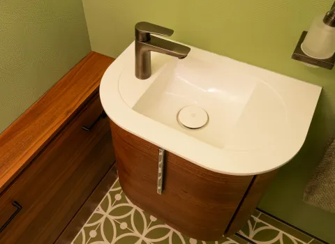 Waschbecken mit Holzunterschrank und grünem Fliesenboden im Gäste-WC.