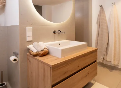 Holzwaschtisch mit Aufsatzbecken und rundem LED-Spiegel im modernen Bad.