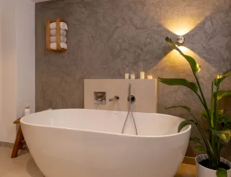Freistehende Badewanne mit dekorativer Wandbeleuchtung und Pflanzen im Badezimmer.