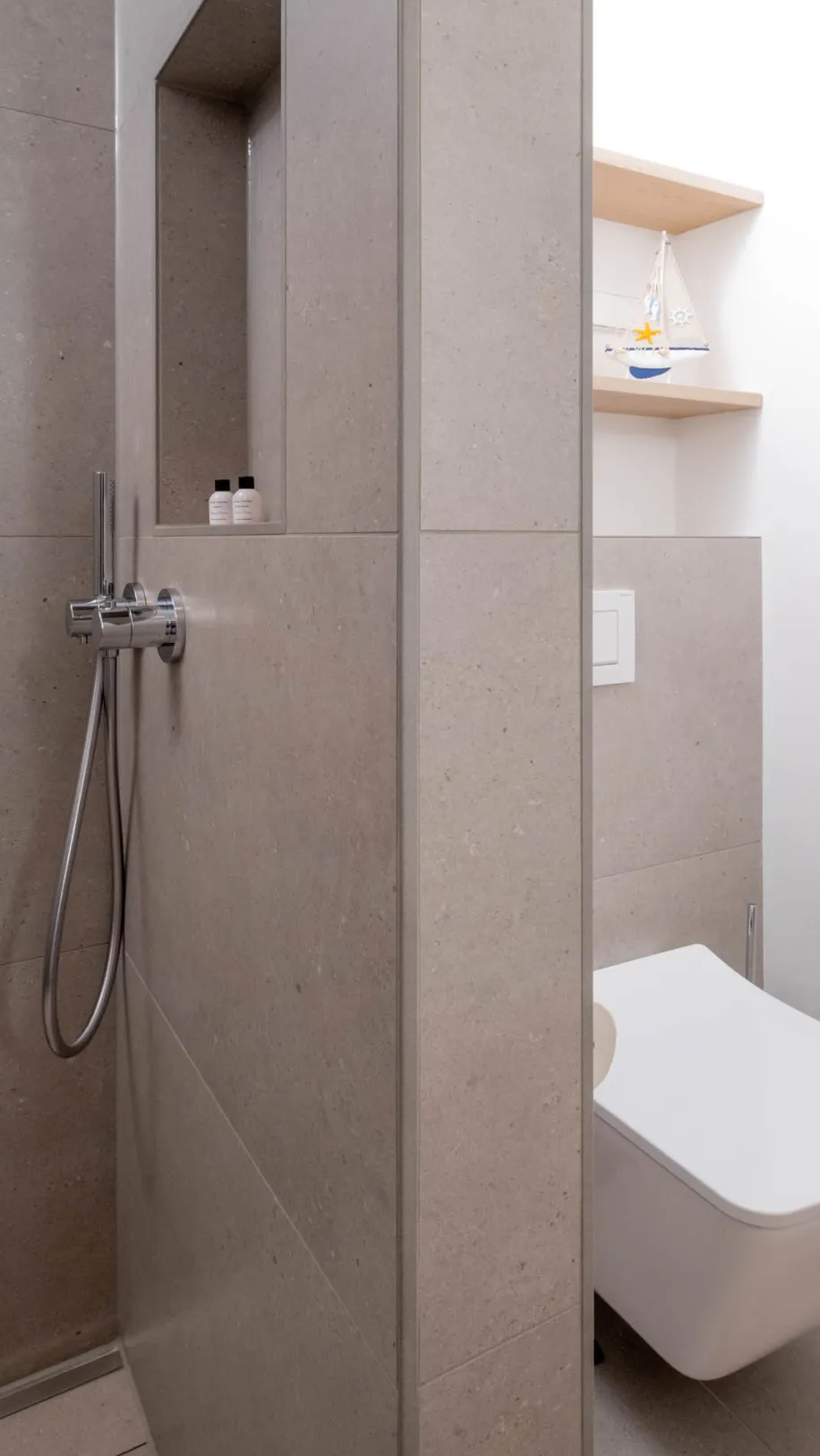 Detailansicht von Duscharmatur mit Wandnische und wandhängendem WC im modernen Bad.