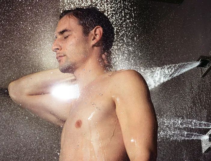 Ein Mann mit geschlossenen Augen steht unter einer Dusche mit Seitenbrausen, die seinen Körper von allen Seiten mit Wasserstrahlen erfrischen.